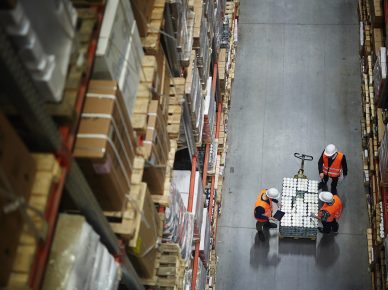 Above view of people working in large warehouse, counting goods on moving cart between shelves with packed boxes