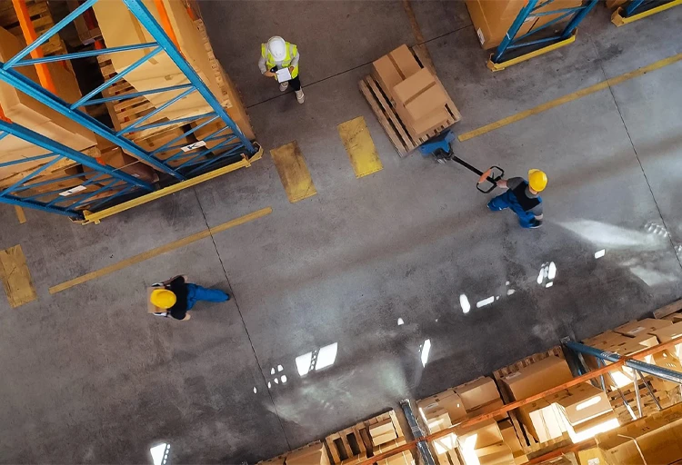 Warehouse workers moving boxes with a pallet jack, minimizing risk of strains, sprains, and other work-related ergonomic injuries.