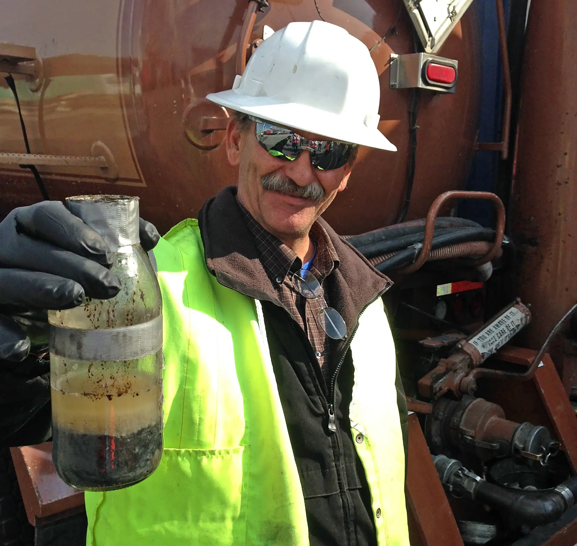 An Apex employee dressed in PPE holding up a soil sample on site during groundwater creosote sampling at the Port of Los Angeles Harbor Department.