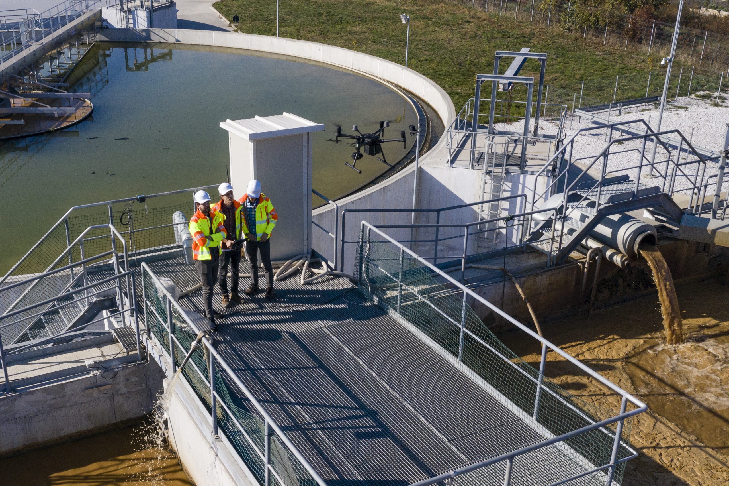 Three employees in PPE flying a drone at a wastewater management site.