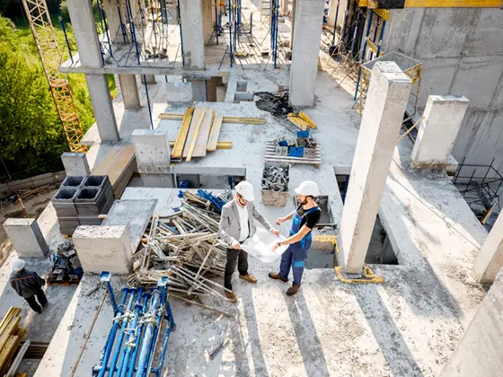 Construction workers on a real estate and financial services job site discussing blueprints.