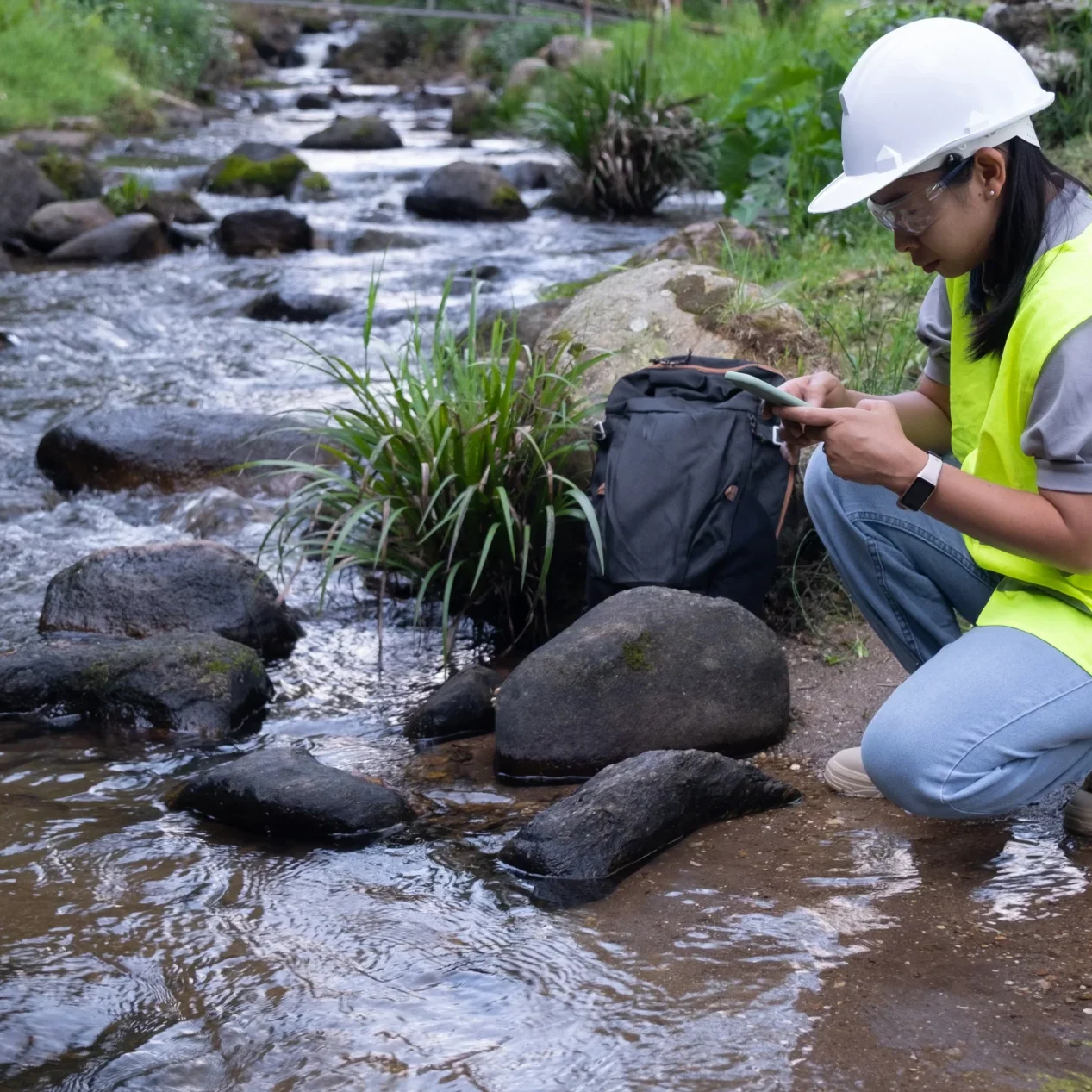 Water engineer with survey equipment kneeling by a stream collecting data