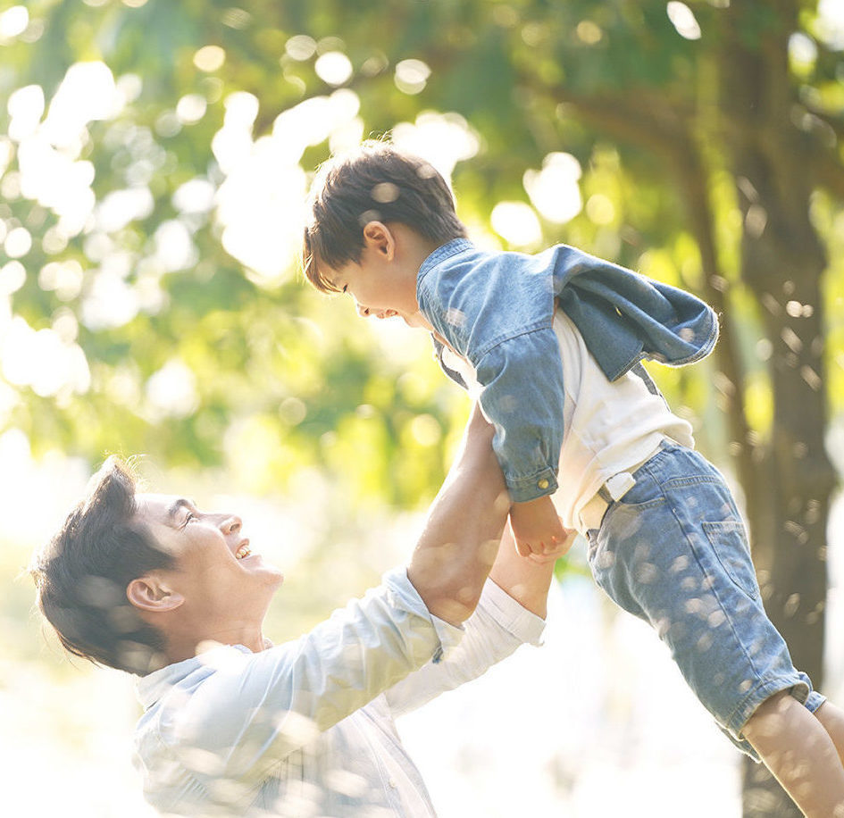happy asian father and son cute little asian boy lifted by father outdoors in park