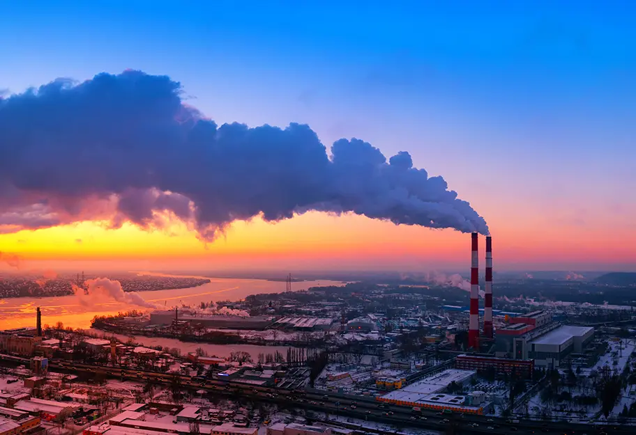 Greenhouse gases, which are subject to emissions reporting, flowing from a plant’s smokestack over an industrial area at dusk