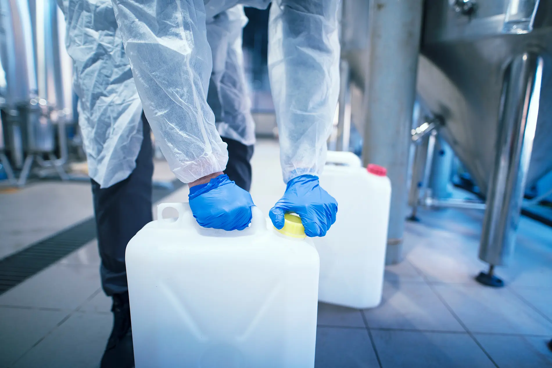 A worker in an industrial facility, following Apex’s process safety management program, wearing protective gloves while handling containers of highly hazardous chemicals.